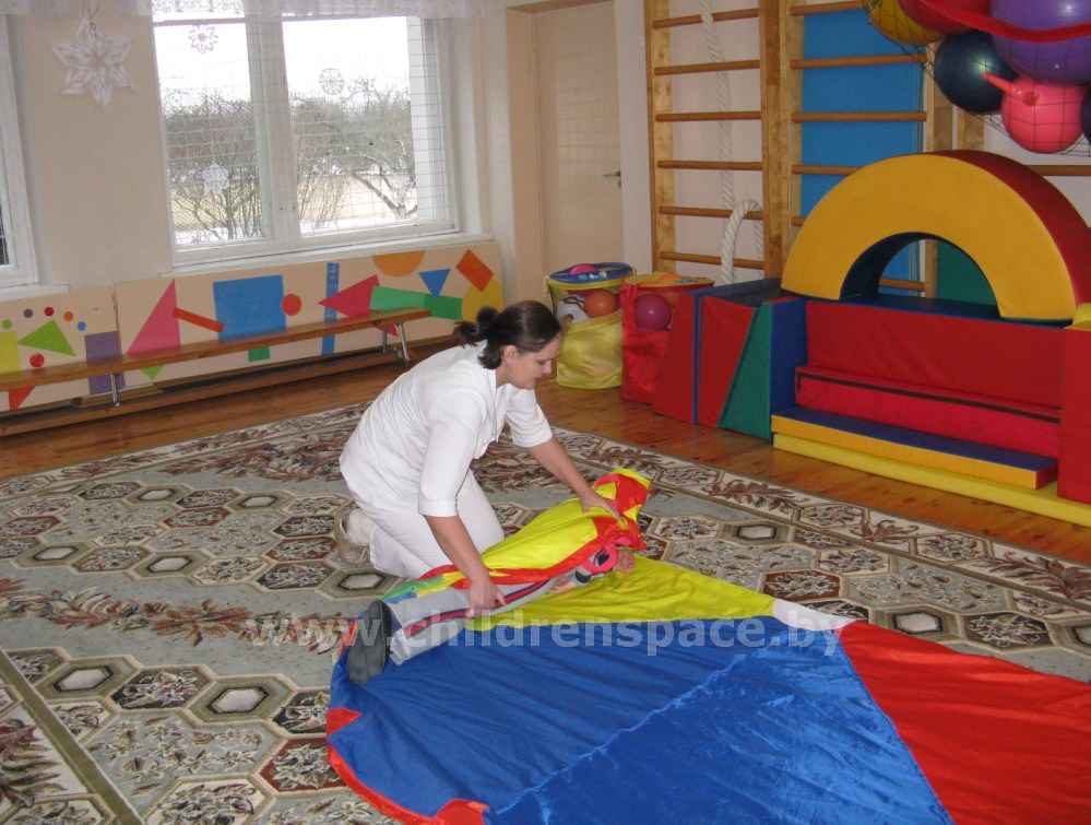 эрготерапевт  заворачивает ребёнка  в  ковёр